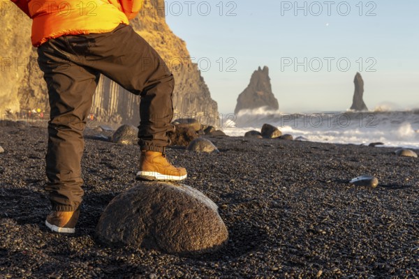 A person is standing on a rock on a beach. The beach is rocky and the sky is blue