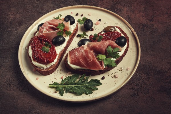 Sandwiches with cheese and prosciutto, dried tomatoes and olives, breakfast on a plate