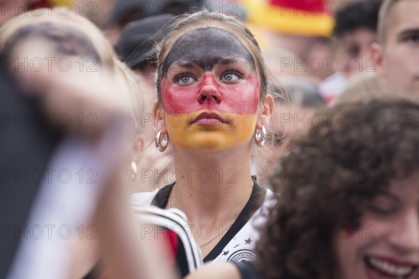 A woman wearing make-up in the German national colours watches the football match in the fan zone at the Brandenburg Tor during the quarter-final match between Germany and Spain at the European Football Championship, Berlin, 05.07.2024