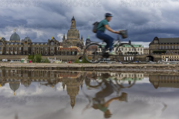 The Dresden silhouette with a cyclist and dark clouds behind the Church of Our Lady is reflected in a puddle on the Elbe cycle path, Elbe cycle path, Dresden, Saxony, Germany, Europe