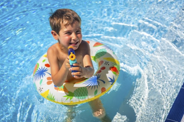 Boy playing with water gun and rubber ring inside the pool