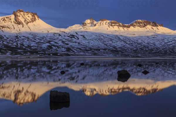 Snow-covered mountains reflected in a fjord in the evening light, Berufjördur, East Fjords, Iceland, Europe