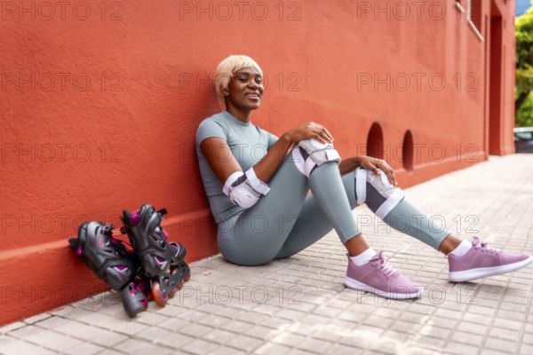 Beautiful african woman roller skating resting sitting on ground and leaning on red facade during the day