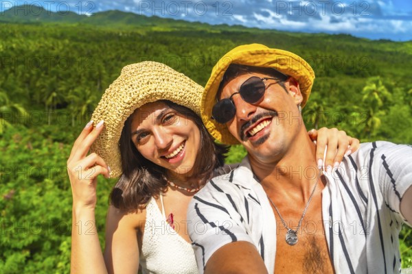 Young couple smiling and taking a selfie with a tropical forest in the background during their vacation in siargao island, philippines