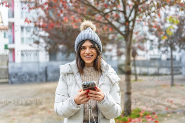 Happy caucasian young woman in warm clothes using phone in the city in winter