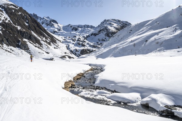 Ski tourer in the snow by a mountain stream in the Funtauna Valley, Graubünden Haute Route, Albula Alps, Rhaetian Alps, Graubünden, Switzerland, Europe