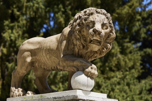 A stone lion statue holding a ball with a forest in the background, Rodini Park, Municipal Park, Rhodes Town, Rhodes, Dodecanese, Greek Islands, Greece, Europe