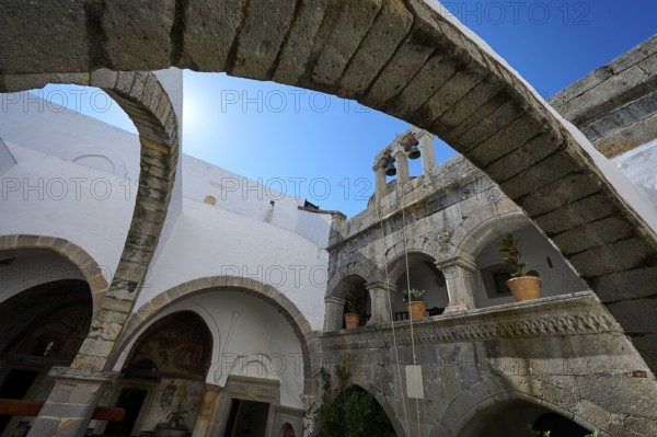 Historic monastery courtyard with stone arches, a tower and hanging plants. Impressive architectural details under a blue sky, Inside the monastery, Agiou Theologou Monastery, Chora, Patmos, Dodecanese, Greek Islands, Greece, Europe