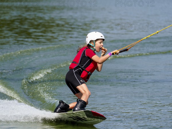 Boy or girl with wakeboard in lake, eating bread, water sports, water skiing in wakepark