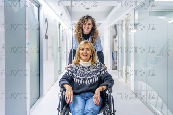 Happy nurse carrying mature female patient in wheelchair at the hospital corridor
