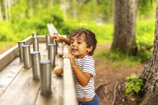Young child exploring and interacting with a sensory play station in a natural park setting, enjoying outdoor activities