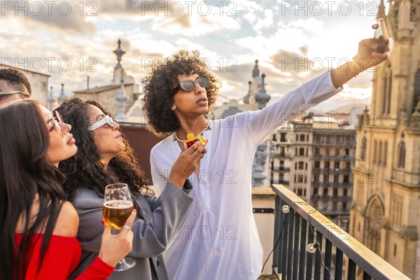 Young man taking selfie with two beauty women in rooftop party with city views during sunset