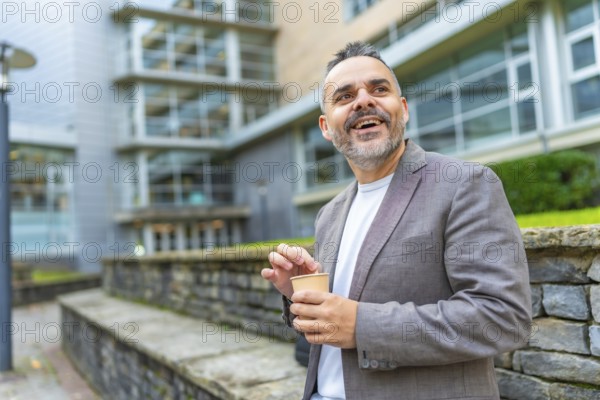 Happy mature caucasian businessman enjoying coffee break outside the block office in the city