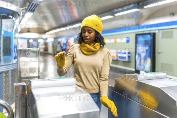 Young black woman wearing yellow winter clothes validating electronic ticket to access subway station