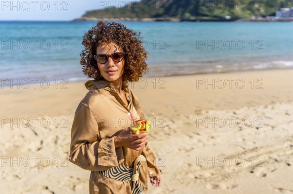 Arab beauty woman in casual summer clothes walking along beach with fresh fruit glass