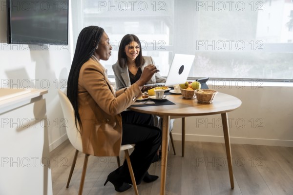 Two businesswomen having breakfast and working on a laptop in their hotel room during a business trip