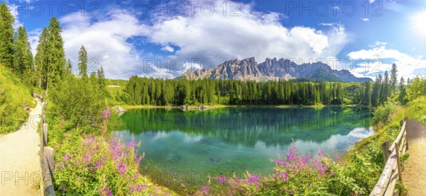 Panoramic view of the beautiful lake carezza with the latemar mountain range in the background on a sunny summer day