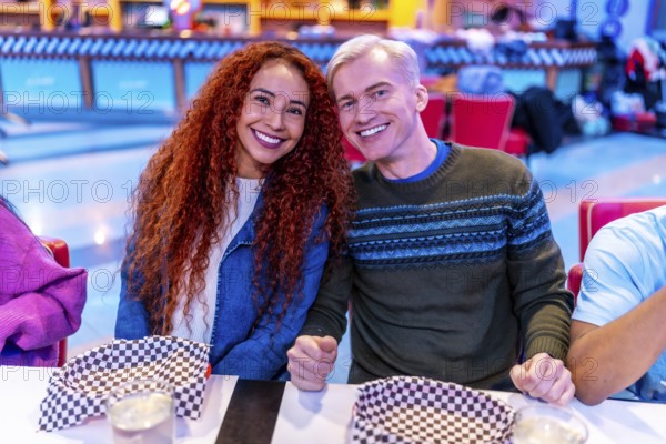 Young multiethnic friends enjoying a meal together at a bowling alley restaurant, celebrating their weekend leisure time