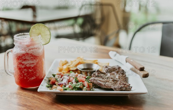 Skirt steak nicaraguan with salad and drink strawberry lemonade served on wooden table. Delicious homemade steak with fries and strawberry lemonade