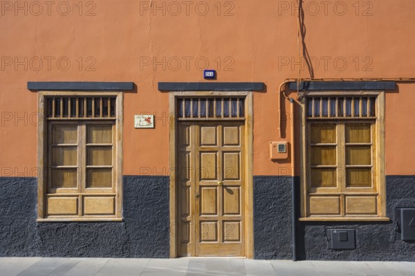 A building facade with an orange wall, wooden door, and windows. The base is painted black, creating a minimalistic urban look, Puerto de la Cruz, Tenerife, Canary Islands, Spain, Europe