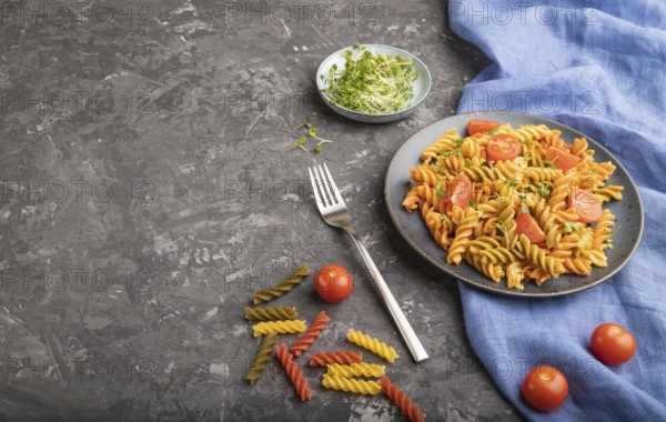 Tortiglioni semolina pasta with tomato and microgreen sprouts on a black concrete background and blue textile. Side view, copy space