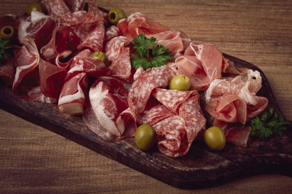 Assortment, sliced meat appetizer, prosciutto, salami and ham, with olives, on a wooden board, breakfast, top view, close-up, no people