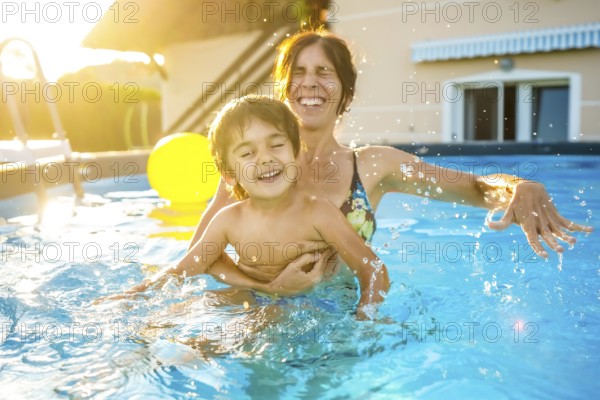 Mother and son are playing and laughing together in a home swimming pool during a sunny summer vacation day