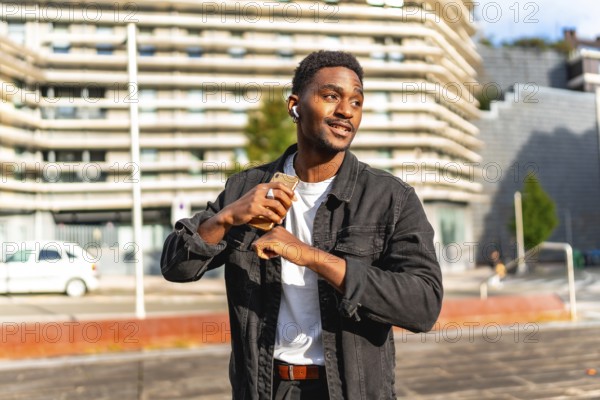 African man listening to music using small wireless earbuds and dancing in the city