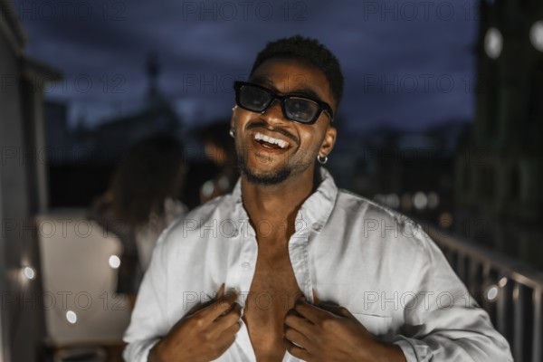 Latin brunette sensual man in sunglasses dancing during night party in a rooftop with multi-ethnic friends
