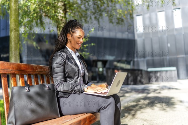 Hispanic elegant businesswoman sitting on city bench working with laptop in the financial district