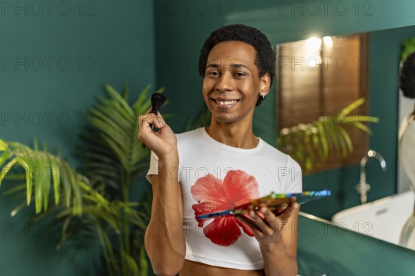 Happy latin young cute gay man holding a makeup palette smiling at camera in the bathroom