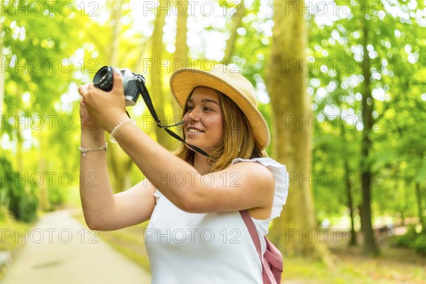 Young female photographer making photos in nature standing in the middle of footpath among green trees