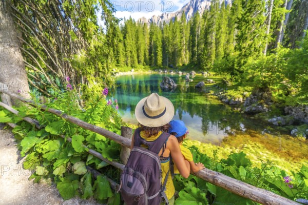 Mother and child enjoying breathtaking view of lake carezza's turquoise waters, surrounded by lush greenery and the majestic dolomites