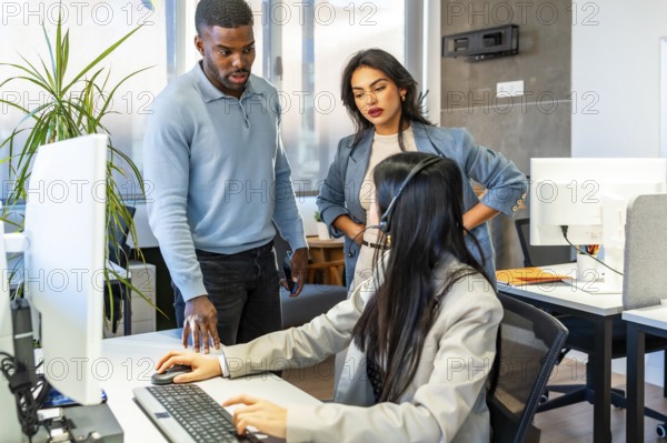 Office workers assisting a colleague using a computer and wearing a headset, possibly working in a customer service or telemarketing