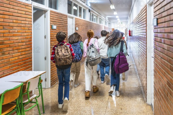 Rear view of elementary school students running down school hallway between classes, carrying backpacks