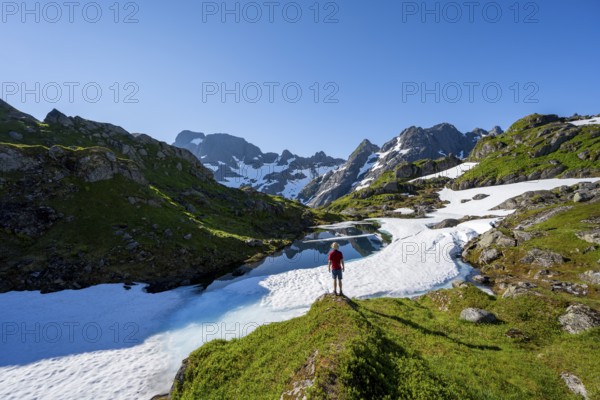 Mountaineer in front of lake with snow remains, Landscape at the mountain hut Trollfjord Hytta, Rocky mountain peaks with snow remains, Mountain landscape at Trollfjord, Lofoten and Vesterålen, Nordland, Norway, Europe