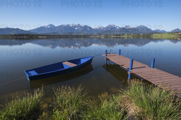 A jetty with a blue boat on a quiet lake with an impressive mountain view, Hopfen am See, near Füssen, Ostallgäu district, Swabia, Bavaria, Germany, Europe