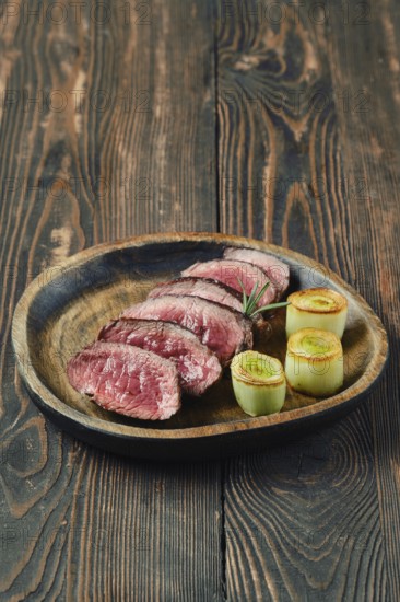 Tender roasted beef slices arranged on a wooden plate, accompanied by artfully presented caramelised leeks