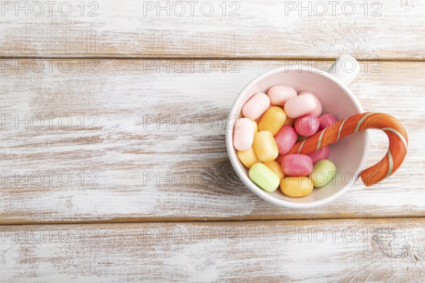 Heap of multicolored caramel candies in cup on white wooden background. copy space, top view, flat lay
