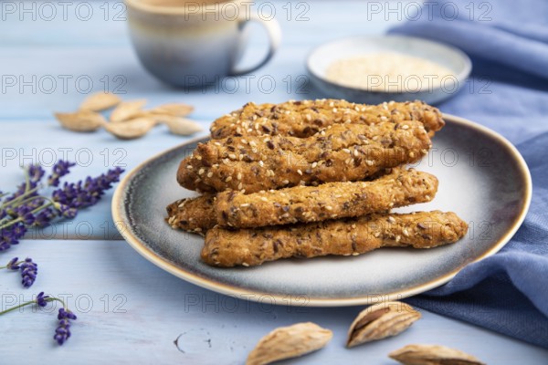 Crumble cookies with seasme and almonds on ceramic plate with cup of coffee and blue linen textile on blue wooden background. side view, close up, selective focus