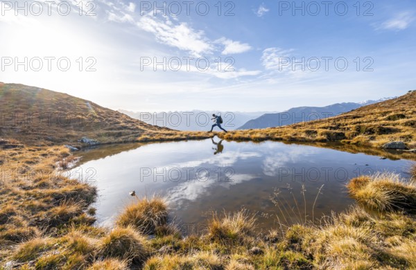 Mountaineer jumping, reflected in a small mountain lake on the Krahberg, mountain panorama in autumn, Venet crossing, Ötztal Alps, Tyrol, Austria, Europe