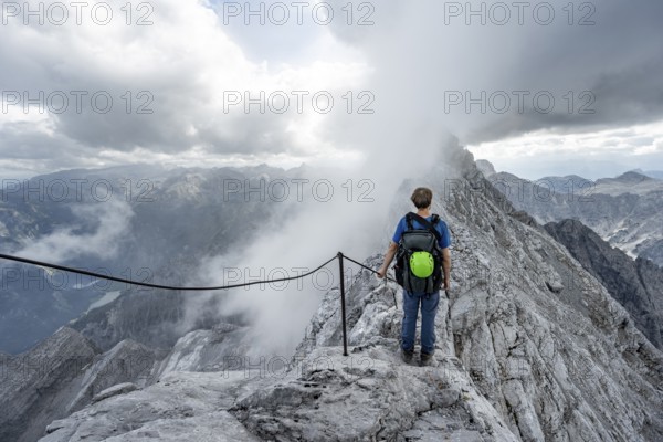 Mountaineer on a narrow rocky ridge on a steel cable, Watzmann crossing to Watzmann Mittelspitze, view of mountain panorama, Berchtesgaden National Park, Berchtesgaden Alps, Bavaria, Germany, Europe
