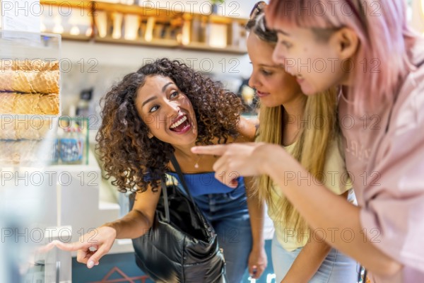 Close-up side view of three excited woman choosing ice cream flavor from counter