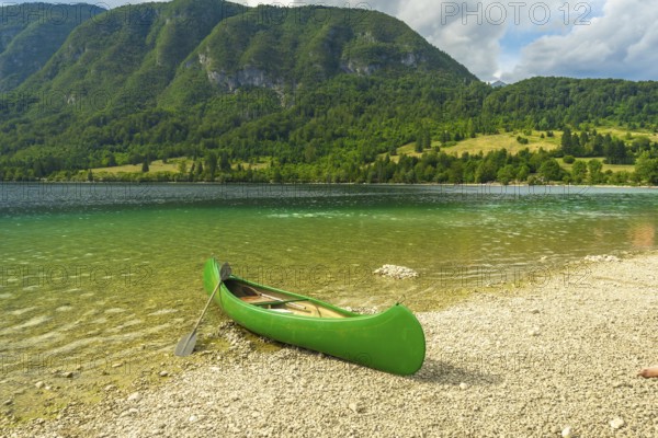 Green canoe sits on the pebbled shore of lake bohinj, inviting visitors to explore the stunning slovenian landscape