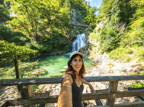 Woman taking selfie with waterfall and turquoise colored water of tolmin gorges in the background, triglav national park, slovenia