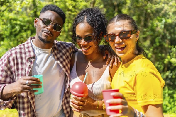 Three cheerful friends are having fun together outdoors, enjoying refreshing drinks on a sunny summer day