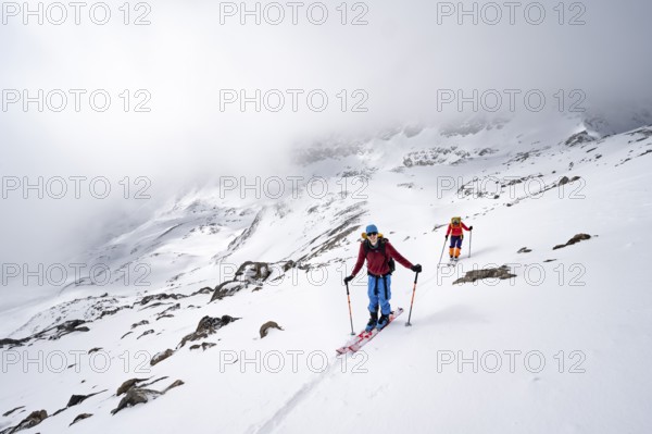 Two ski tourers in a wintry mountain landscape with cloudy mountain peaks, ascent to Piz Laviner, Grisons Haute Route, Albula Alps, Rhaetian Alps, Grisons, Eastern Switzerland, Switzerland, Europe