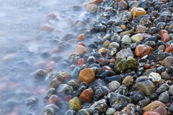 Blurred sea water of wave rolling over wet colourful pebbles on shingle beach, cobble beach