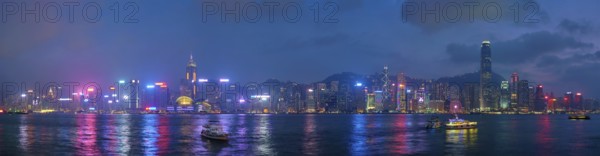 Panorama of Hong Kong skyline cityscape downtown skyscrapers over Victoria Harbour in the evening illuminated with tourist boat ferries, Hong Kong, China, Asia
