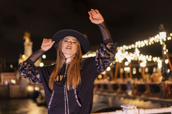 Christmas lights in the city, Caucasian blonde girl dressed in black with a hat on an illuminated bridge, winter lifestyle